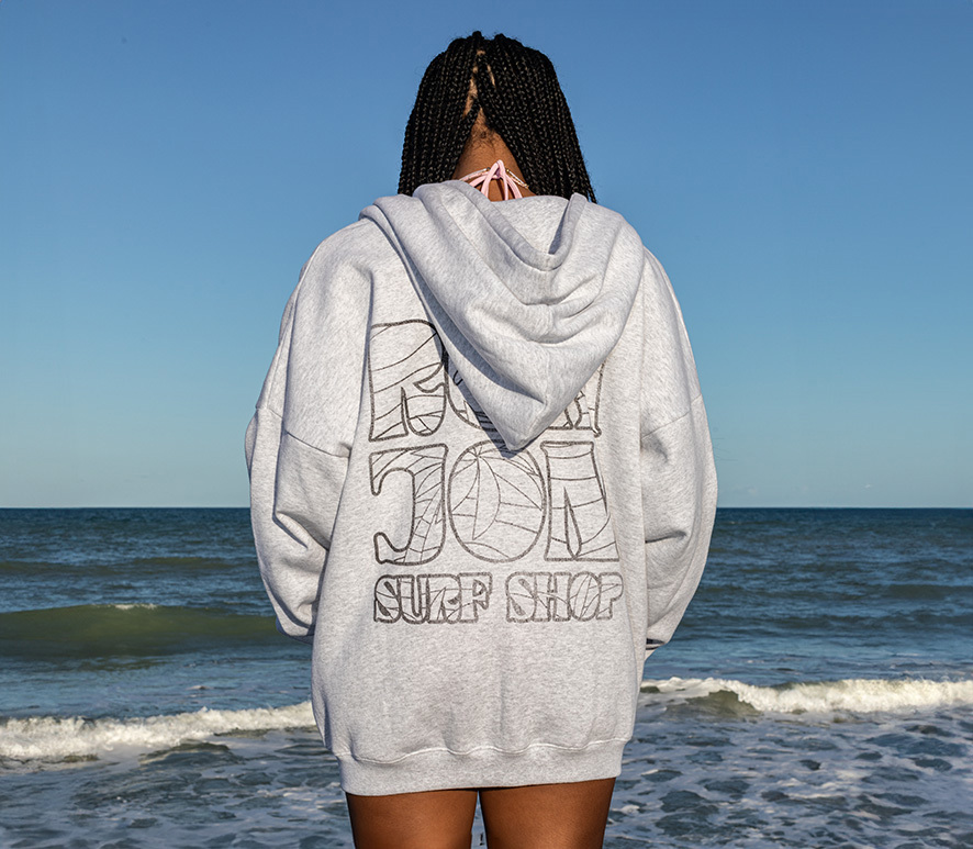 girl in a grey hoodie standing on the beach looking at the water