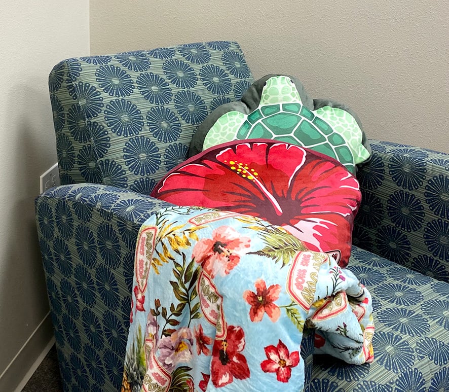 apolstered chair with a soft blanket across one arm and tropical themed pillows leaning against the other arm