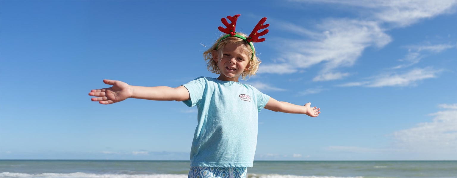 young child wearing novelty antlers standing on the beach with arms outstretched