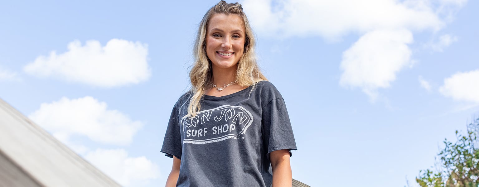 woman wearing ron jon tee shirt with blue sky and white clouds behind her