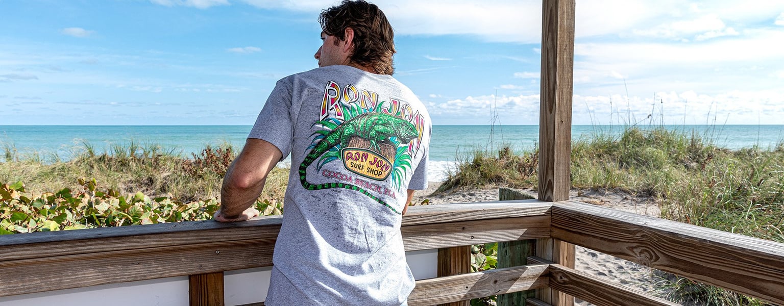 guy standing in a beach pavilion looking at the beach with an iguana graphic on his shirt