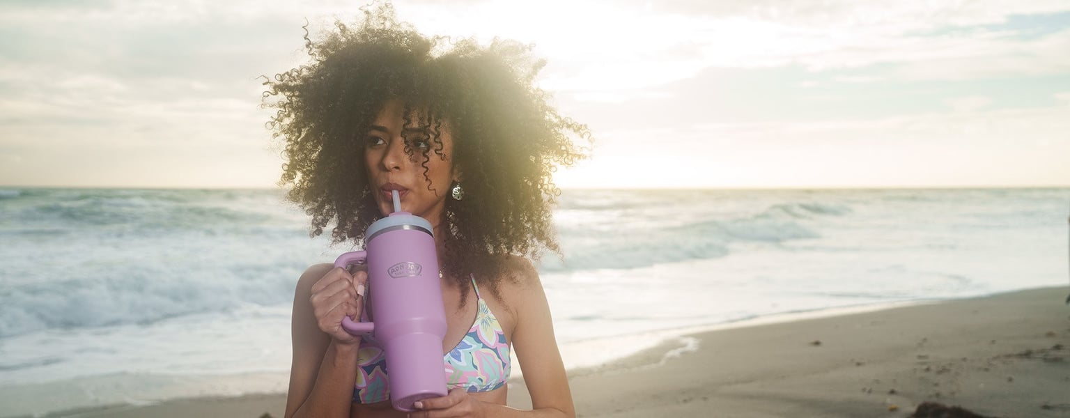 woman on the beach drinking from an insulated tumbler