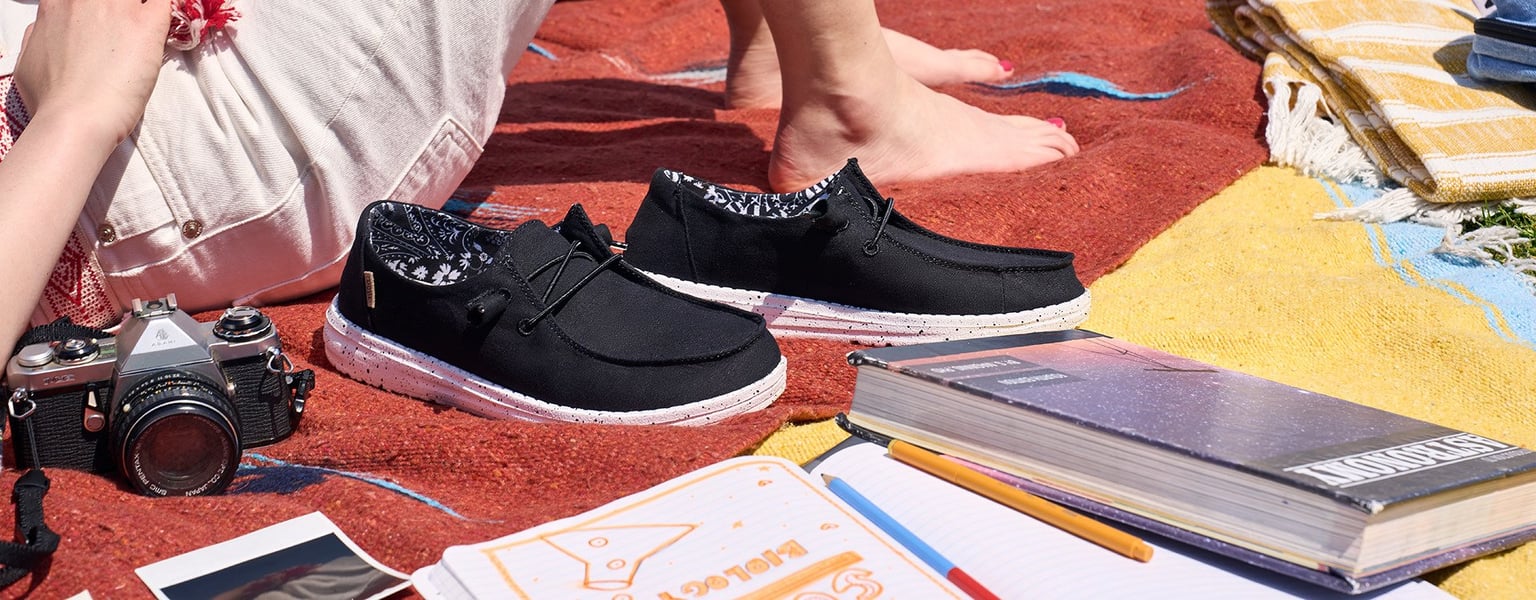 a person relaxing on a blanket outdoors with their shoes, camera, and books around them