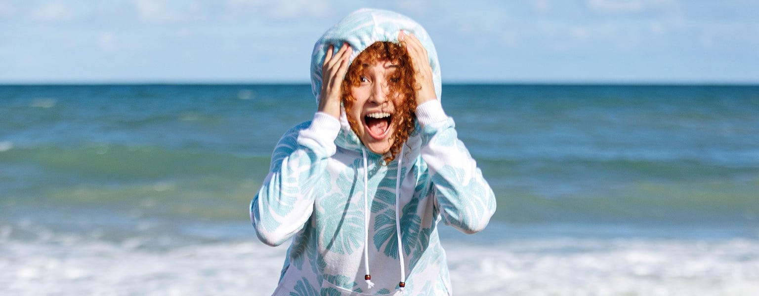 woman at the beach wearing a hoodie leaning toward the camera with a shocked look