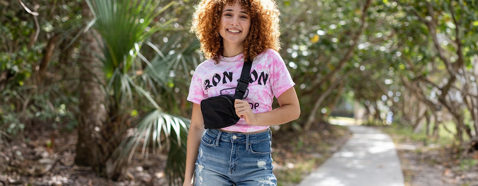 girl with red curly hair carrying a black hip bag over her shoulder