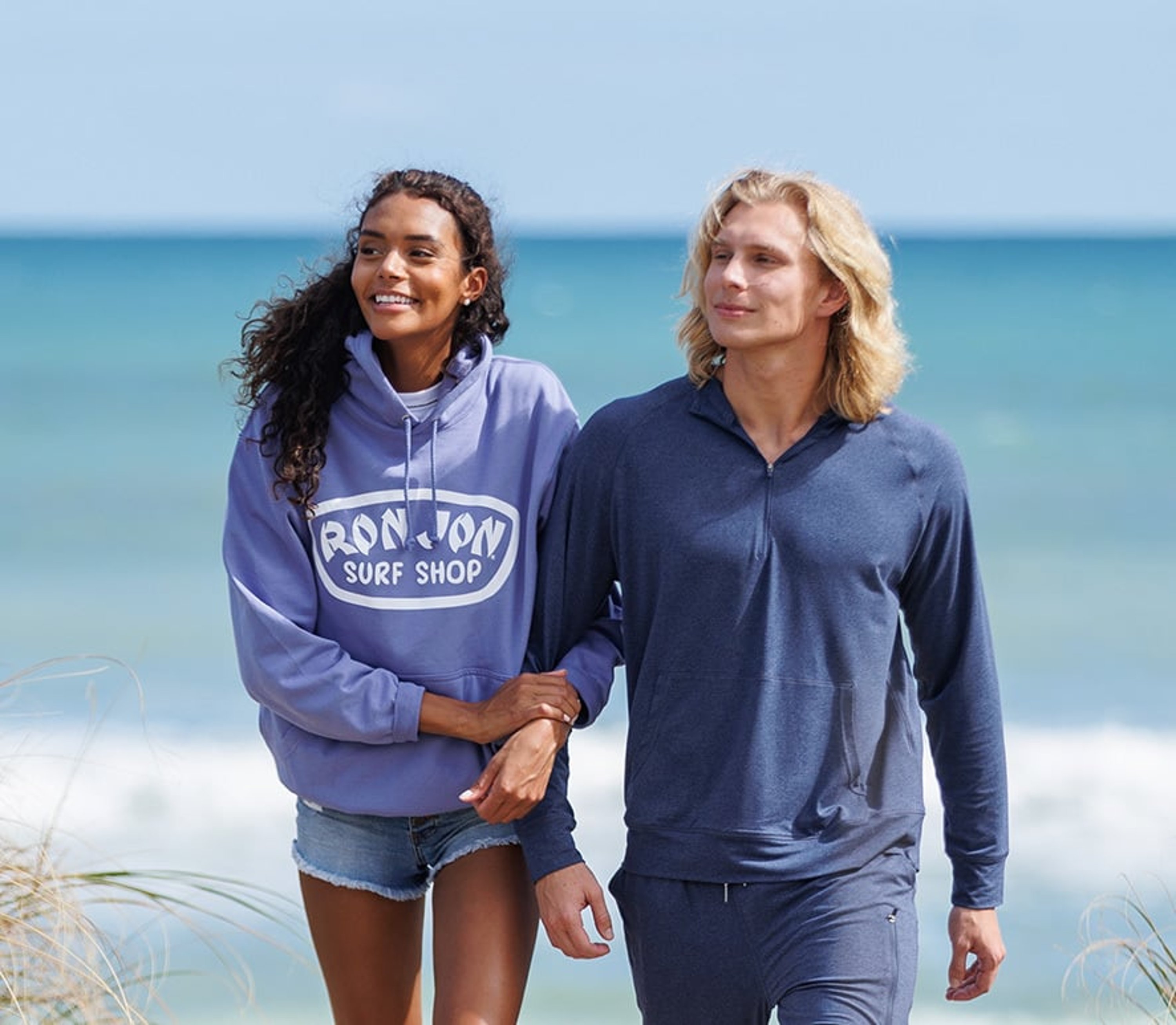 couple walking on the beach wearing long sleeve hooded tops