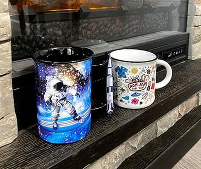 two ceramic mugs sitting on the hearth of a fireplace