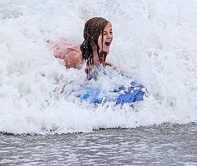young girl rides a bodyboard as the wave breaks around her