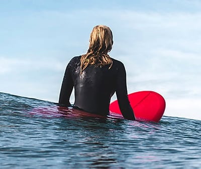 surfing wearing a long-sleeve wetsuit sitting on a red surfboard with their back to the camera