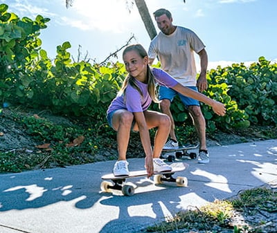 father teaching their daughter how to skateboard