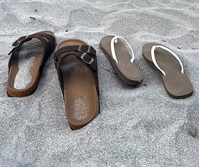 a pair of mens sandals and womens sandals sitting on the sand at the beach