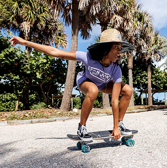girl riding a skateboard wearing a large brim straw lifeguard hat