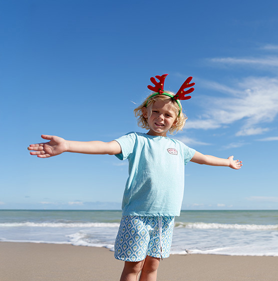 young child on the beach wearing a ron jon tee shirt and novelty antlers