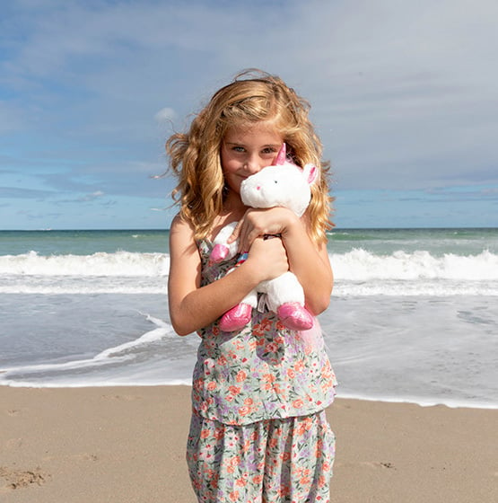 young girl at the beach hugging a plush unicorn