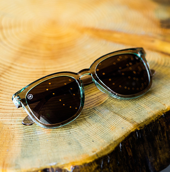 Green-rimmed sunglasses with dark lenses rest on a circular, polished wooden surface with visible rings and light reflections.