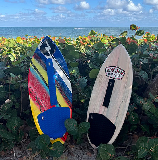 two skimboards with traction accessories installed among foliage at the beach