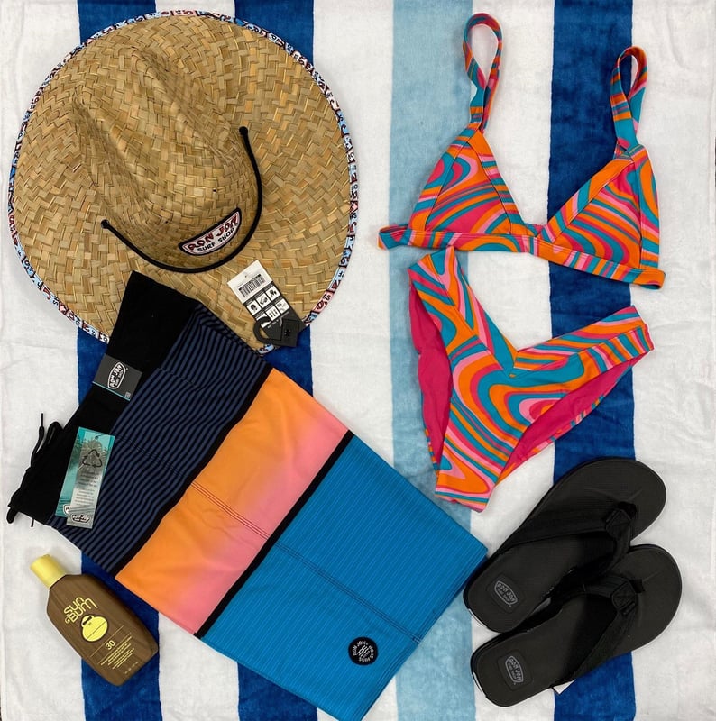 Photo of beach hat boardshorts bikini sandals and sunscreen on towel